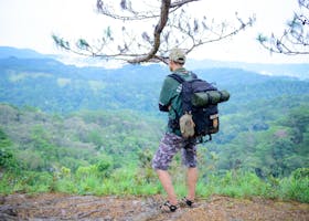 A man with a backpack stands on a cliff, admiring scenic mountain views.