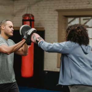 Boxing training indoors with coach guiding punch techniques to trainee.